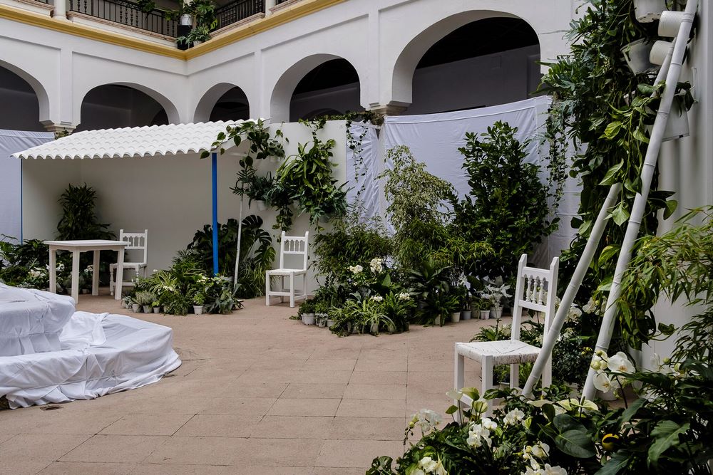 Patio blanco con sillas y mesas blancs y plantas verdes con flores blancas