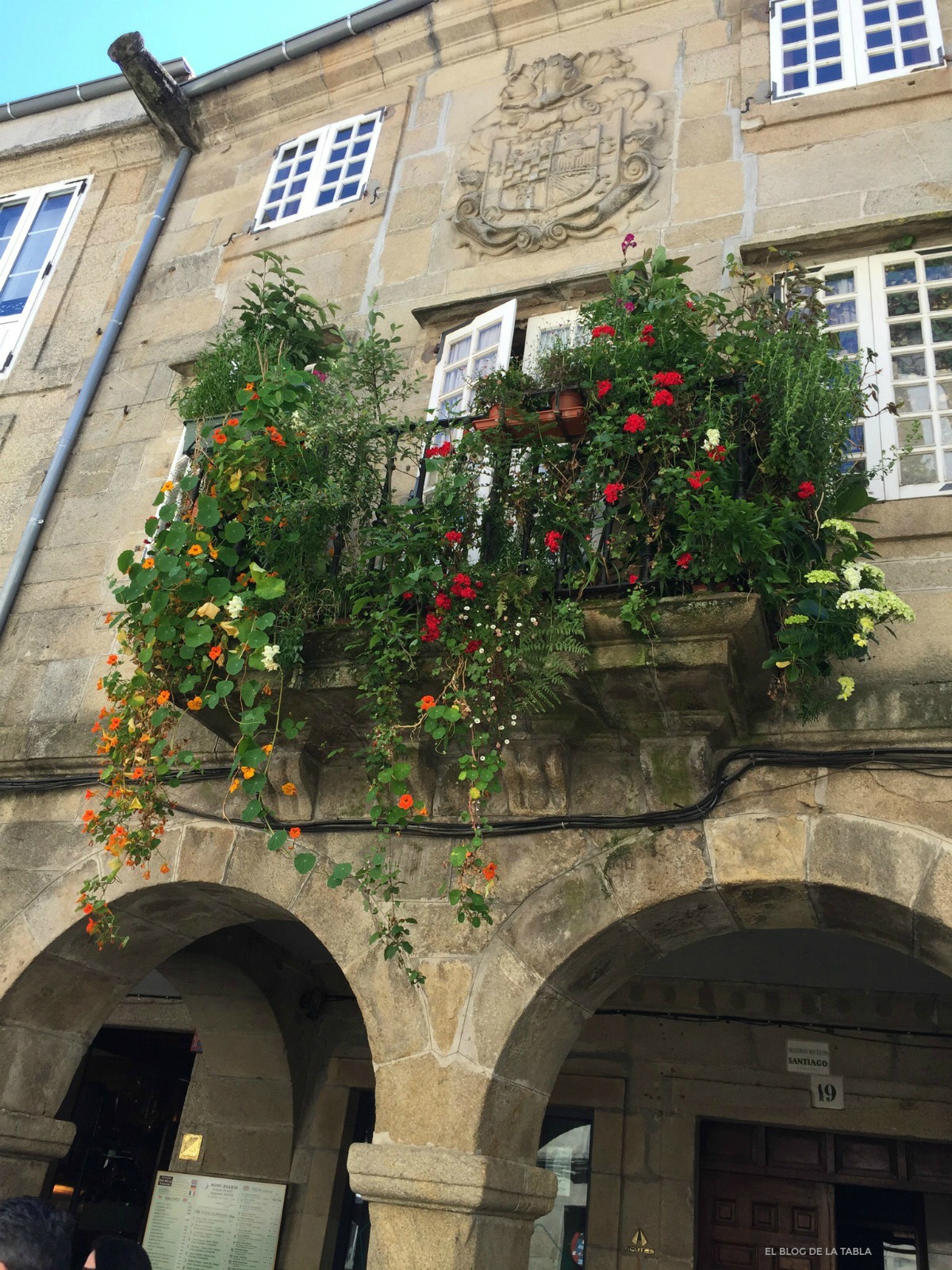 Fachada de piedra, soportales y balcon con plantas y flores