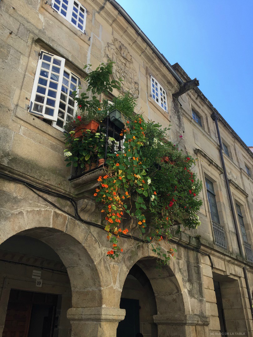 Fachada de piedra, soportales y balcón florido en Santiago Compostela