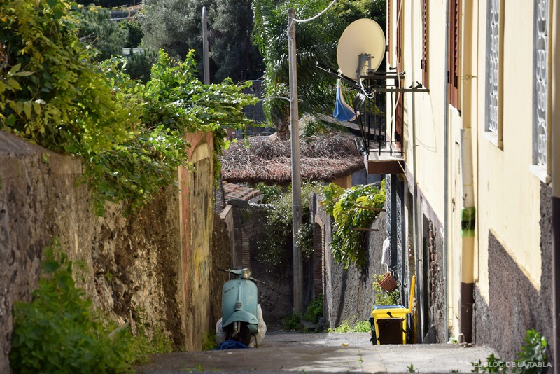 Calle inclinada y moto vespa en un pueblo de Sicilia, Italia