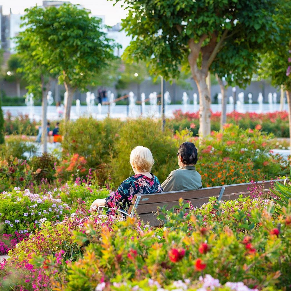 Personas sentadas en un banco rodeado de flores en el Parque Central en Valencia